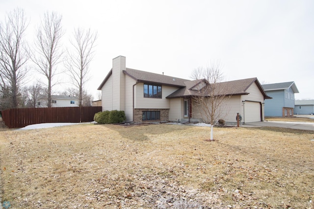 split level home with an attached garage, fence, driveway, and a chimney