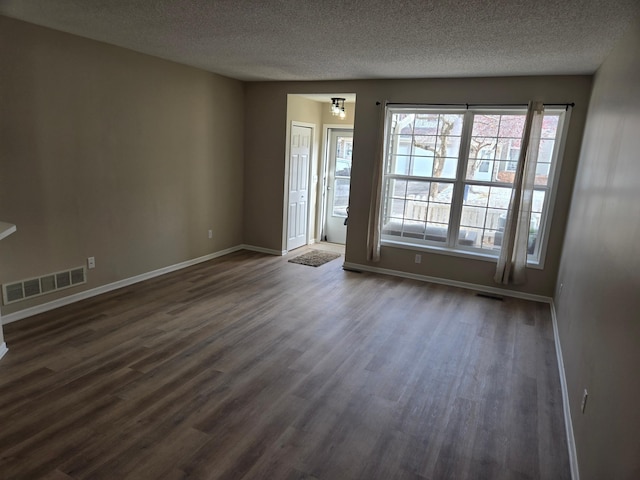 spare room with visible vents, baseboards, a textured ceiling, and dark wood-style flooring