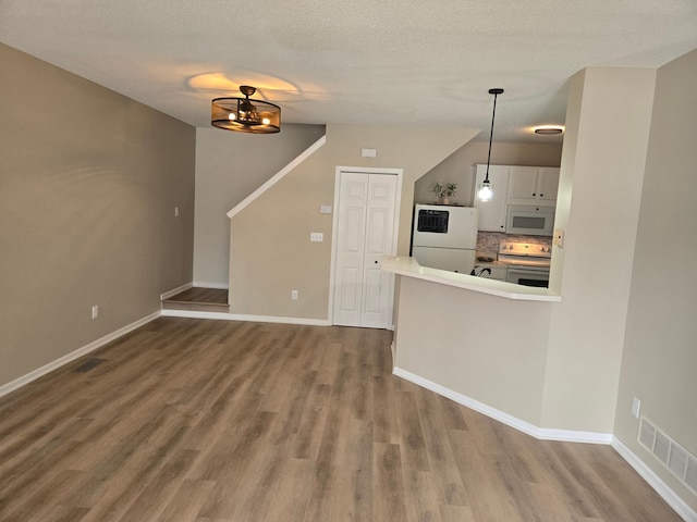 interior space with white appliances, wood finished floors, visible vents, white cabinets, and pendant lighting