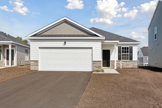 view of front facade with board and batten siding, stone siding, an attached garage, and aphalt driveway