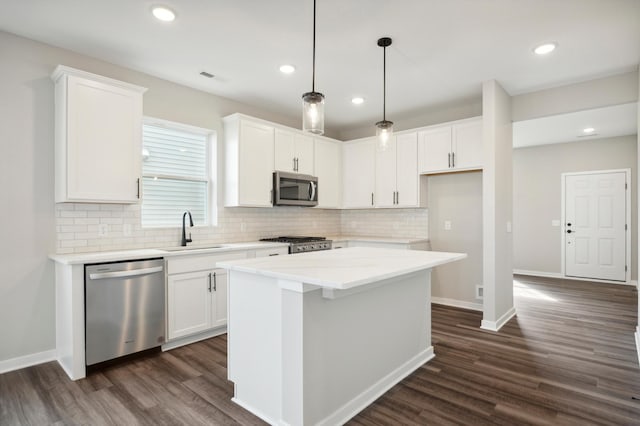 kitchen with white cabinets, dark wood-style floors, a kitchen island, appliances with stainless steel finishes, and a sink