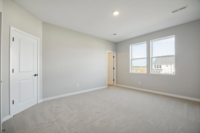 unfurnished room with light carpet, visible vents, and baseboards