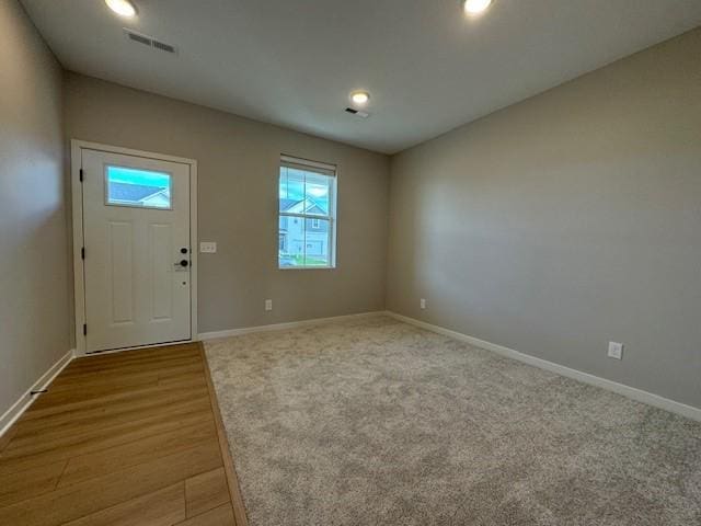 carpeted foyer entrance with wood finished floors, visible vents, and baseboards