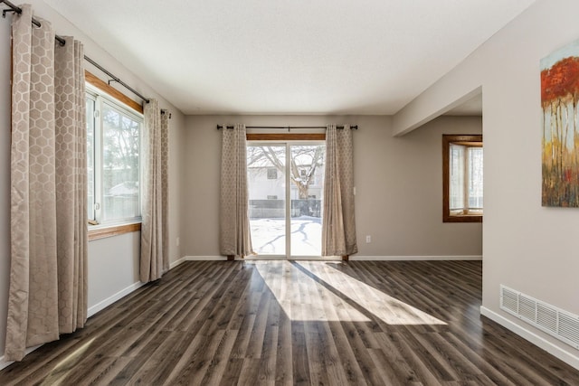 unfurnished room featuring baseboards, visible vents, and dark wood finished floors