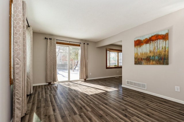 unfurnished room featuring dark wood-style floors, a wealth of natural light, visible vents, and baseboards