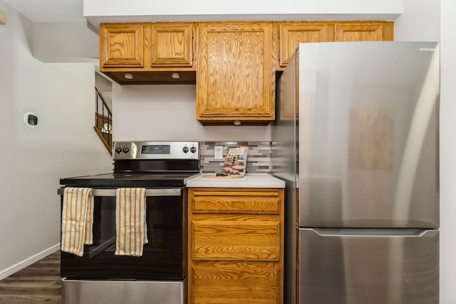 kitchen featuring baseboards, dark wood finished floors, decorative backsplash, stainless steel appliances, and light countertops