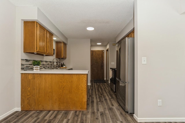 kitchen with a peninsula, light countertops, backsplash, freestanding refrigerator, and brown cabinets