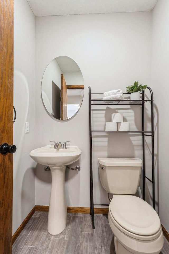 half bath with toilet, baseboards, and wood finished floors