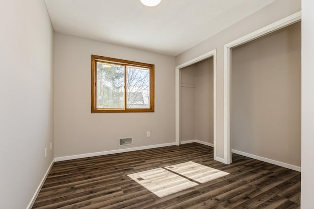 unfurnished bedroom with visible vents, dark wood finished floors, and baseboards