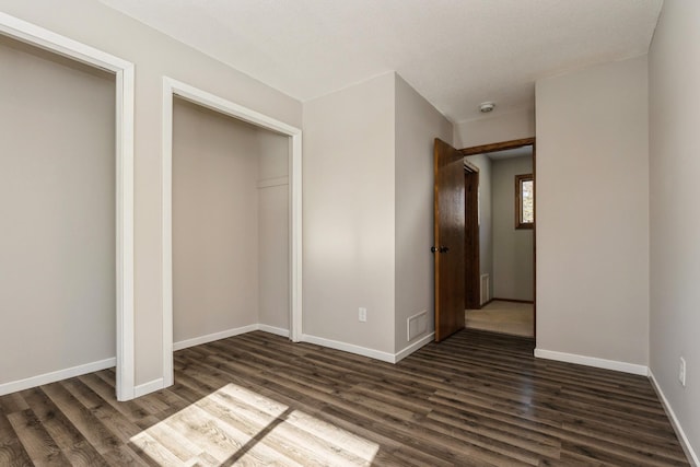 unfurnished bedroom featuring a closet, dark wood-style flooring, visible vents, and baseboards