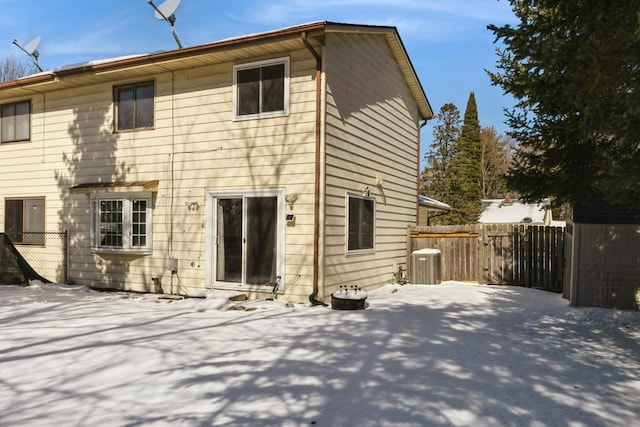 snow covered house featuring central AC unit and fence