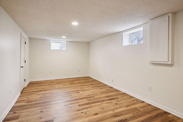 below grade area with recessed lighting, light wood-style flooring, a textured ceiling, and baseboards