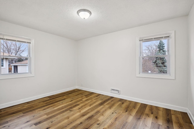 empty room featuring a wealth of natural light, visible vents, baseboards, and hardwood / wood-style flooring