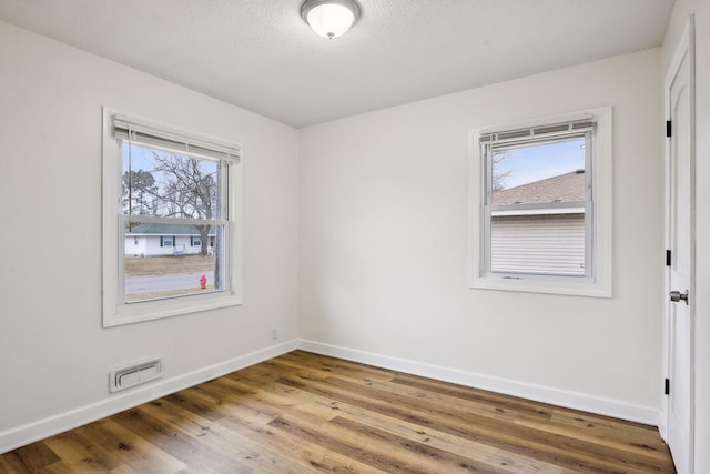 unfurnished room featuring visible vents, a healthy amount of sunlight, baseboards, and wood finished floors