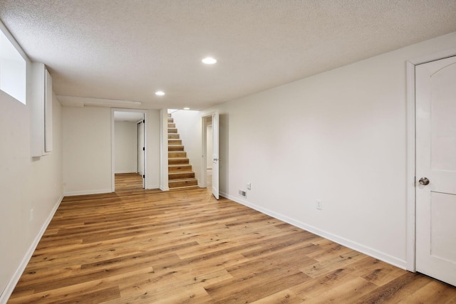 finished basement with baseboards, light wood finished floors, recessed lighting, stairs, and a textured ceiling