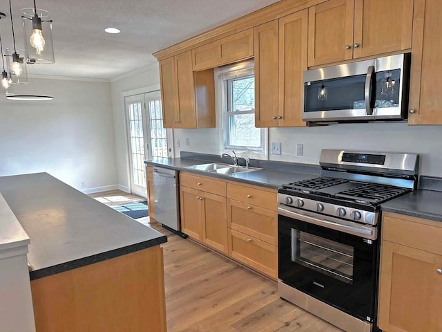 kitchen featuring dark countertops, light wood finished floors, crown molding, appliances with stainless steel finishes, and a sink