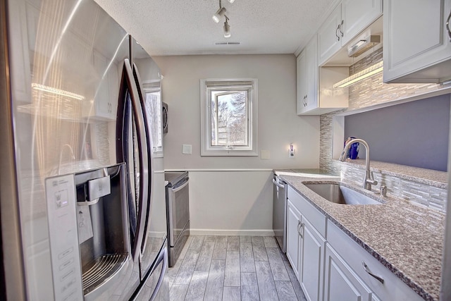 kitchen featuring wood finish floors, light stone counters, stainless steel appliances, a textured ceiling, and a sink