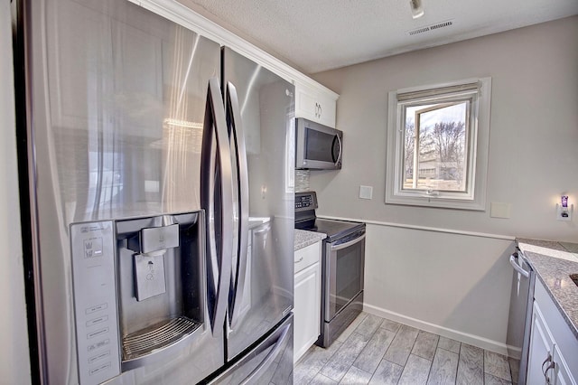 kitchen with visible vents, wood tiled floor, appliances with stainless steel finishes, white cabinets, and a textured ceiling