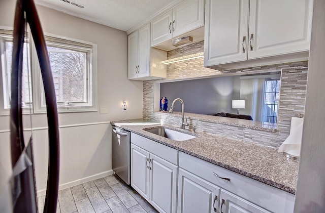 kitchen with a sink, light stone counters, dishwasher, and white cabinetry