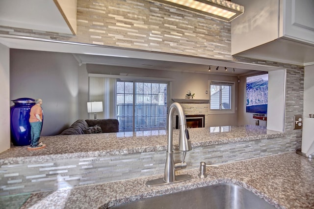 kitchen with open floor plan, stone counters, a sink, and a glass covered fireplace