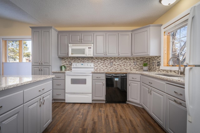 kitchen featuring gray cabinetry, white appliances, a sink, a wealth of natural light, and dark wood-style floors