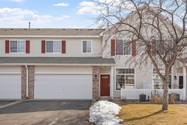 multi unit property featuring a front lawn, an attached garage, driveway, and roof with shingles