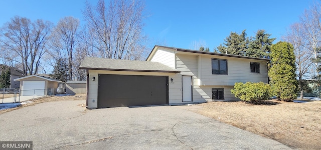 split level home with aphalt driveway, an attached garage, and fence