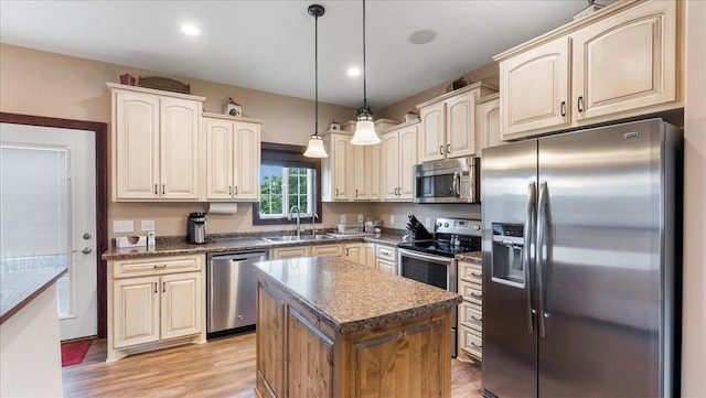 kitchen with light wood finished floors, a sink, stainless steel appliances, dark countertops, and decorative light fixtures