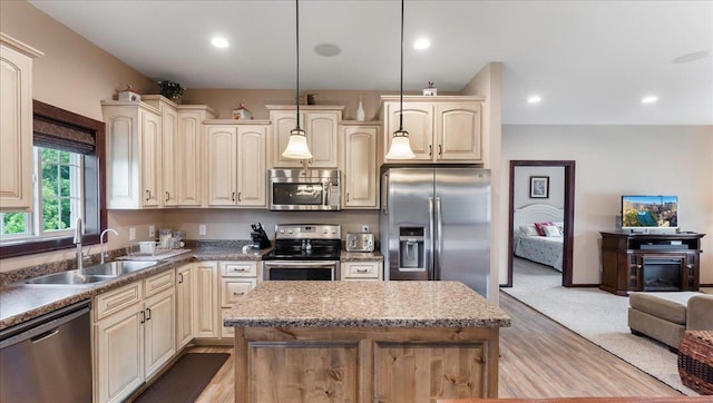 kitchen with cream cabinetry, a sink, open floor plan, a center island, and appliances with stainless steel finishes