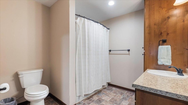 bathroom with vanity, toilet, baseboards, and stone finish flooring