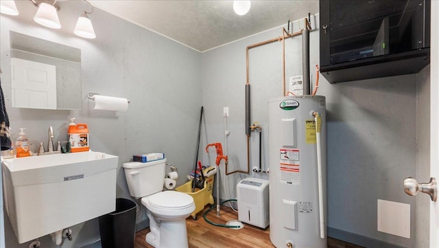 bathroom with a sink, electric water heater, wood finished floors, and toilet