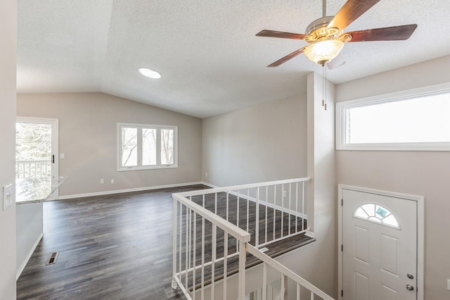 foyer entrance featuring lofted ceiling, a textured ceiling, dark wood-type flooring, visible vents, and baseboards