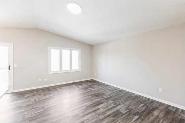 empty room with lofted ceiling, dark wood-type flooring, visible vents, and baseboards