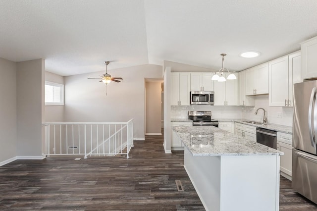 kitchen featuring stainless steel appliances, a kitchen island, a sink, vaulted ceiling, and decorative backsplash