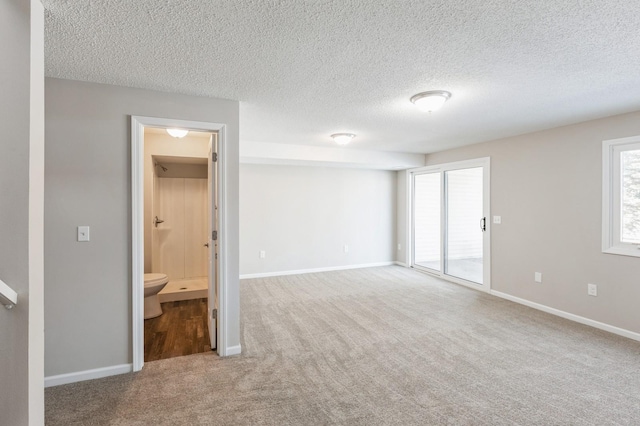 unfurnished bedroom with a textured ceiling, carpet flooring, baseboards, access to exterior, and ensuite bath