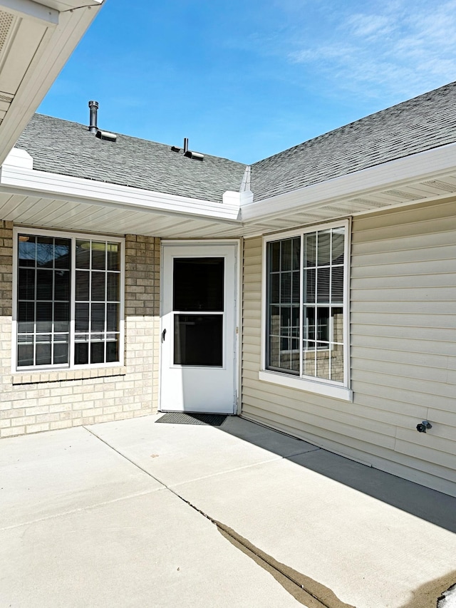 doorway to property featuring a patio area, brick siding, and a shingled roof