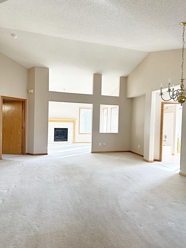 unfurnished living room featuring baseboards, a tiled fireplace, carpet floors, an inviting chandelier, and a textured ceiling