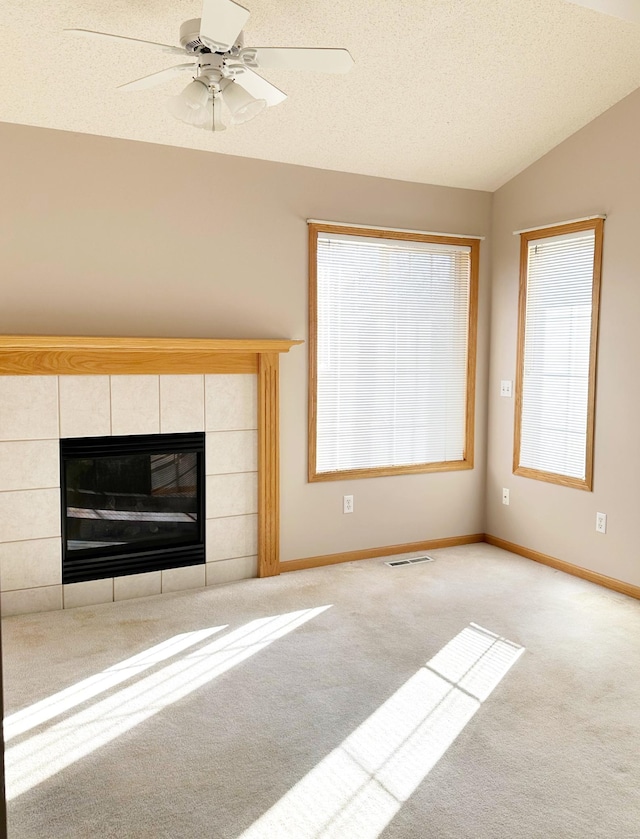 unfurnished living room featuring visible vents, a tiled fireplace, a textured ceiling, carpet, and vaulted ceiling