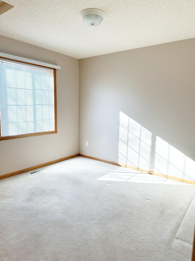 carpeted empty room with visible vents, a textured ceiling, and baseboards