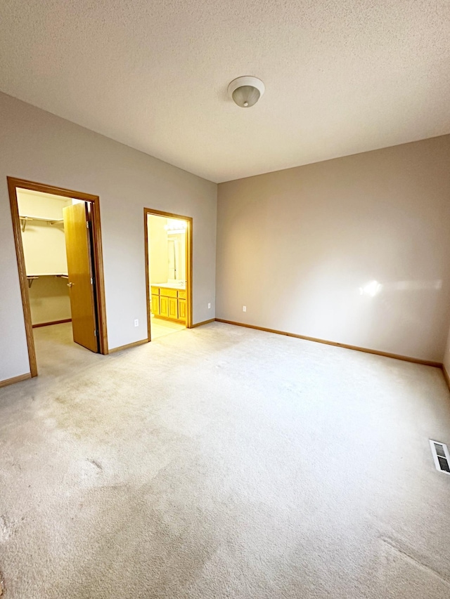 unfurnished bedroom with a spacious closet, light colored carpet, a textured ceiling, and baseboards