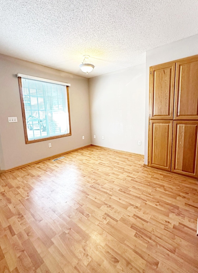 empty room featuring visible vents, light wood-style flooring, a textured ceiling, and baseboards