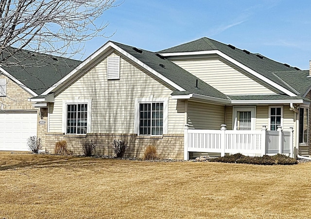 rear view of house with brick siding, a shingled roof, covered porch, a garage, and a yard