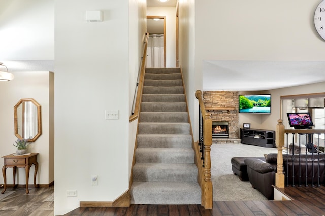 stairs with baseboards, wood finished floors, and a stone fireplace