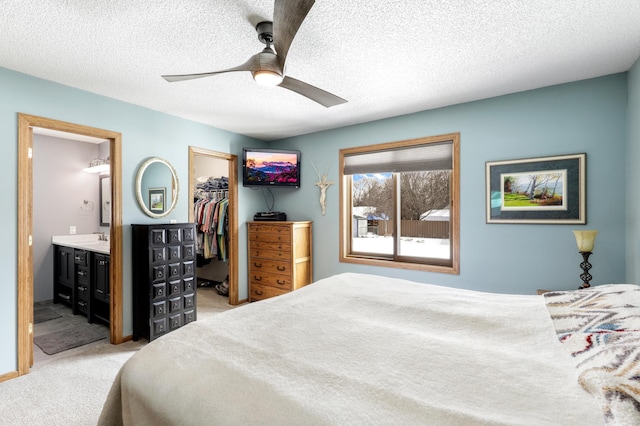 bedroom featuring a walk in closet, a closet, ensuite bathroom, light carpet, and a sink