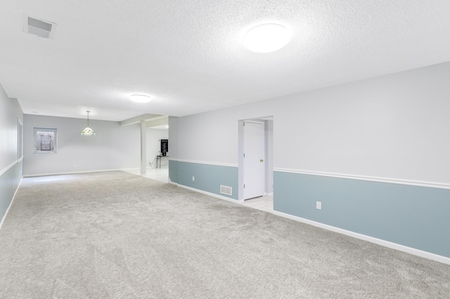 basement featuring light carpet, a textured ceiling, and visible vents