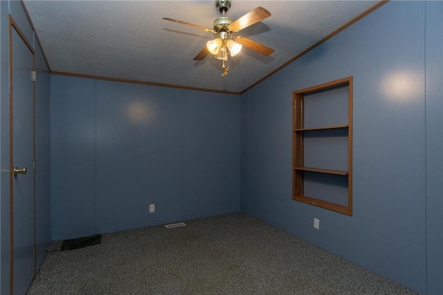 carpeted empty room with built in shelves, ceiling fan, a textured ceiling, and crown molding