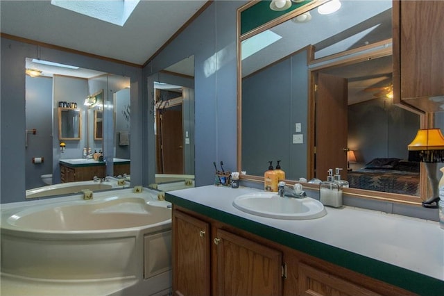 bathroom featuring ornamental molding, vaulted ceiling with skylight, a garden tub, and a sink