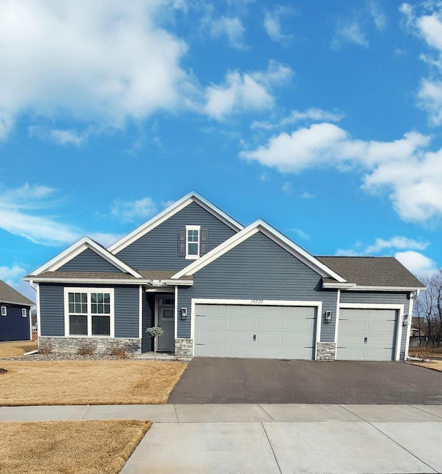 view of front of property with stone siding, driveway, a shingled roof, and a garage