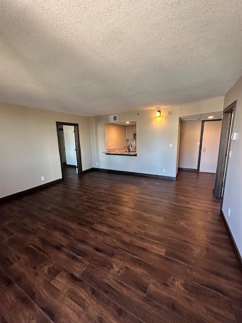 unfurnished living room featuring dark wood finished floors, visible vents, and baseboards