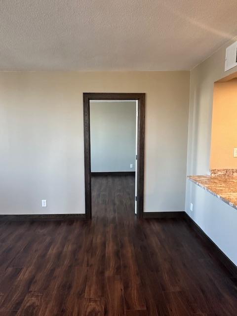 empty room featuring dark wood-style flooring, visible vents, a textured ceiling, and baseboards